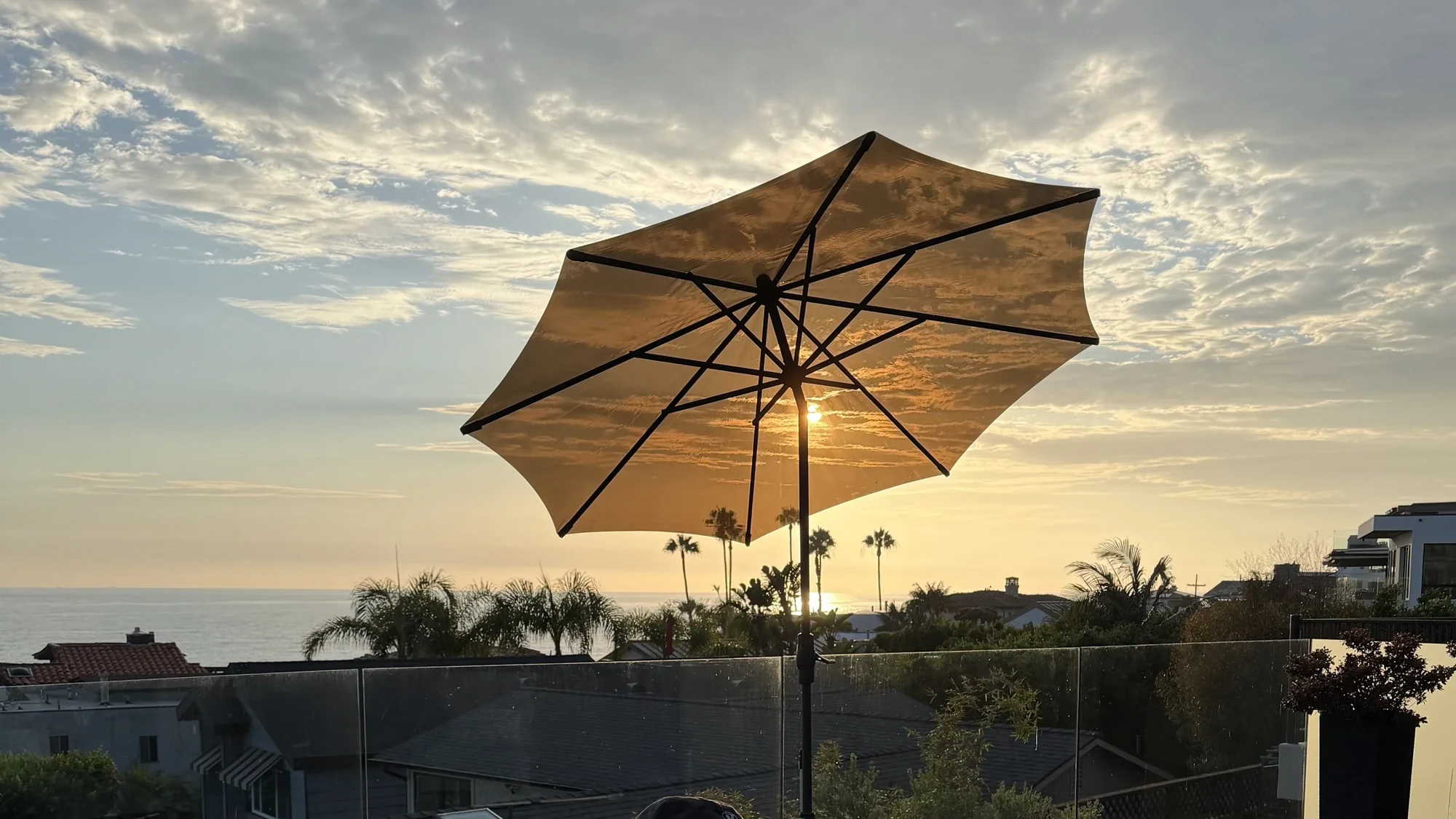 A see-through Sunglass umbrella framing the clouds above an ocean sunset